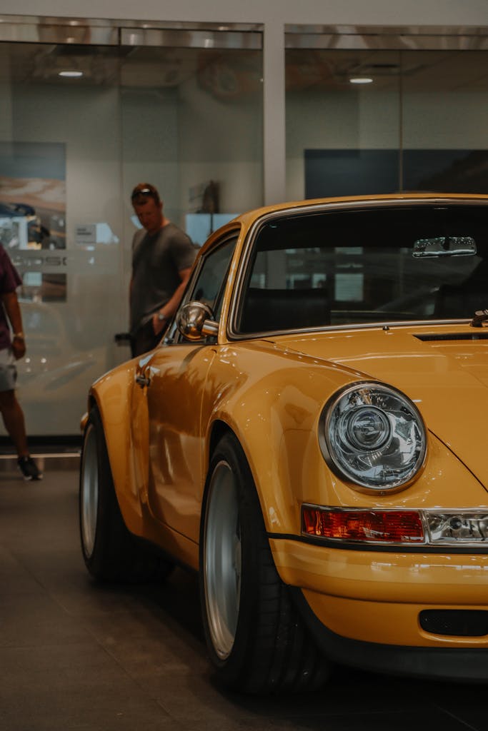 A striking classic yellow Porsche 911 displayed in an indoor car showroom.