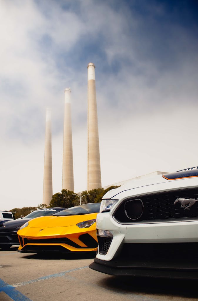 A striking lineup of luxury cars, including a Mustang and Lamborghini, against Morro Bay Power Plant.