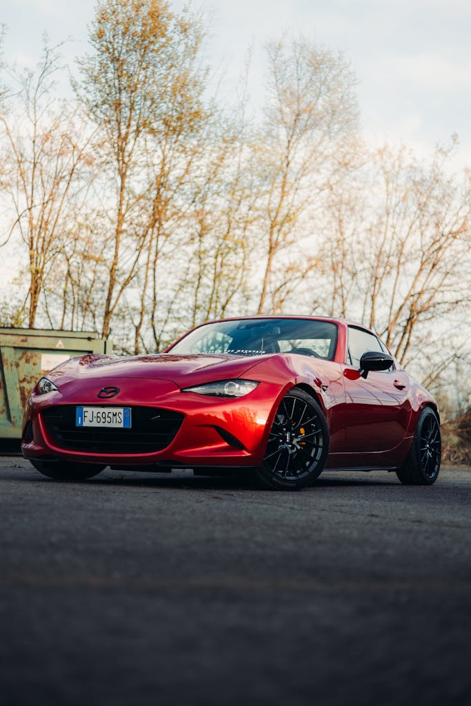 Elegant red sports car under daylight in a serene outdoor setting, perfect for automotive enthusiasts.