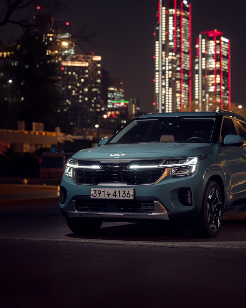 Night view of a Kia SUV parked against a lit city skyline, highlighting urban elegance and design.