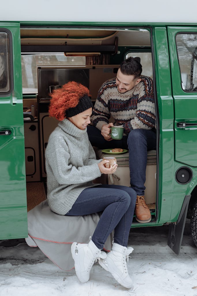 A couple enjoying a warm tea break inside a green camper van during a snowy winter trip.