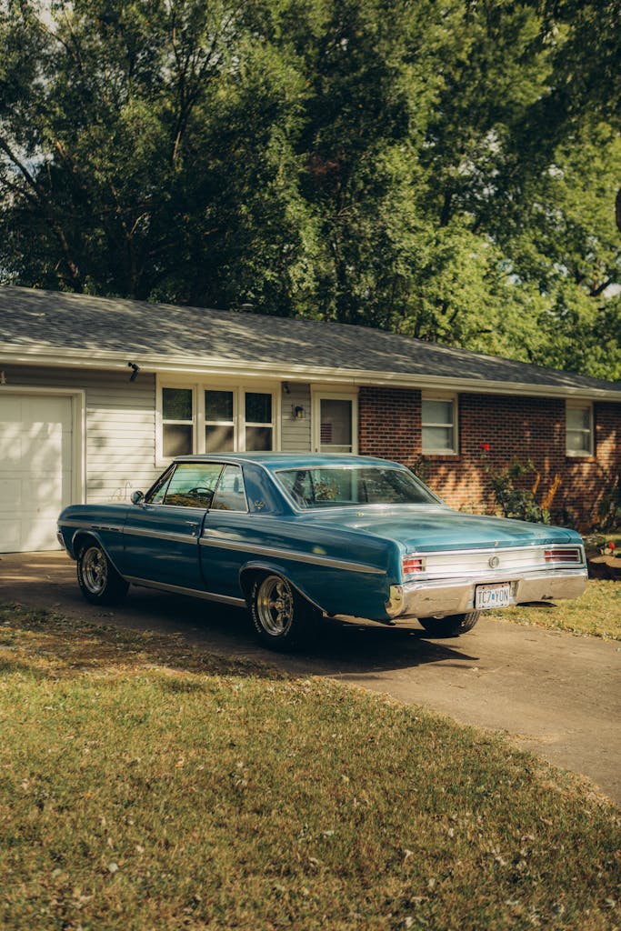 Classic blue car parked in a suburban driveway on a sunny day.