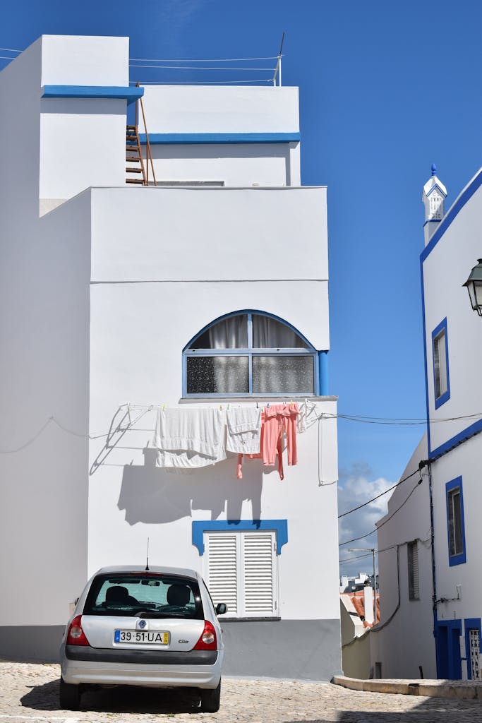 White building with laundry hanging and car parked below in sunny street. Minimalist architectural style.