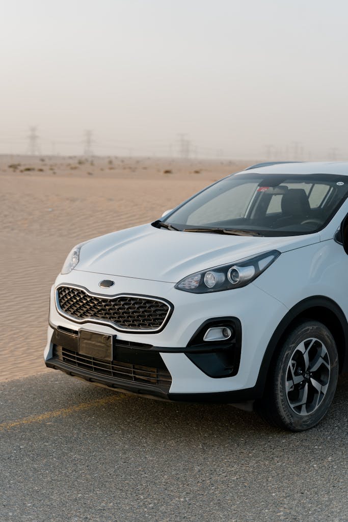 White SUV parked on a desert road with sand dunes in the background.