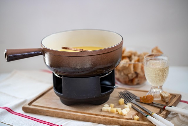 Gruyere Cheese On A Wooden Board With A Knife And Fondue Pot In The Background