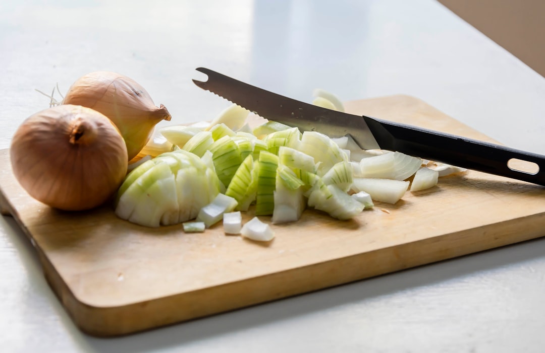 Onions On A Cutting Board With A Knife And Fresh Herbs In The Background