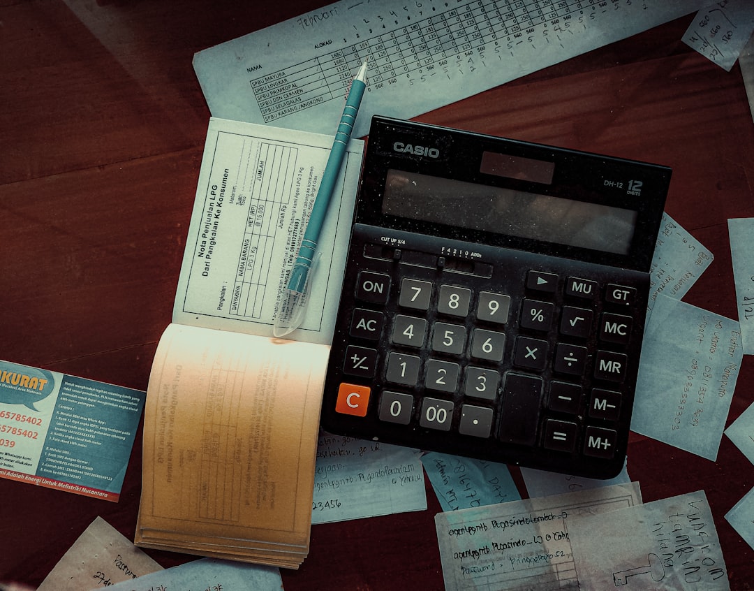 Person Writing A Budget With A Calculator And Financial Documents On A Desk