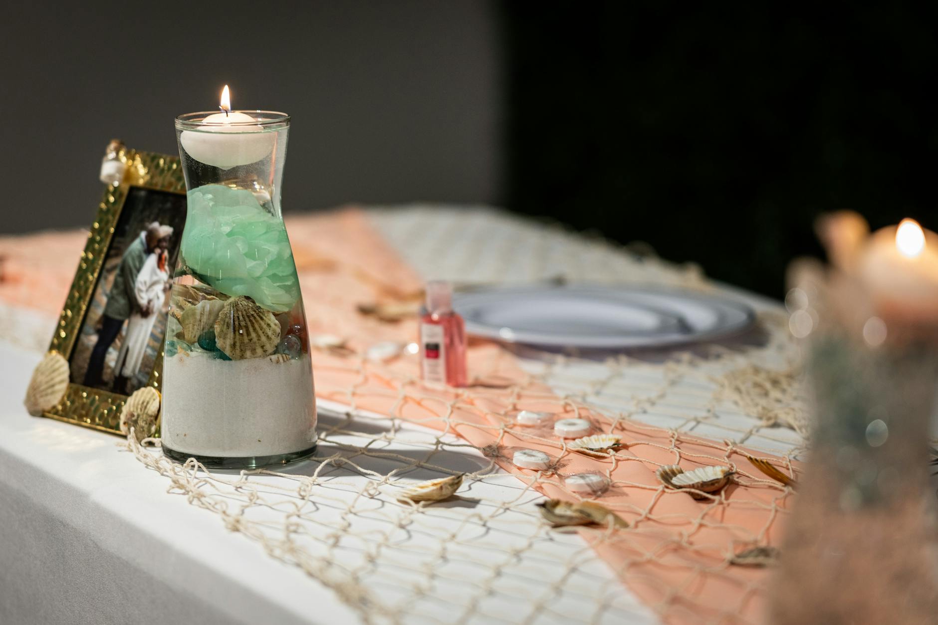 Wide Glass Vase Filled With Sand And Large Seashells With A Pillar Candle