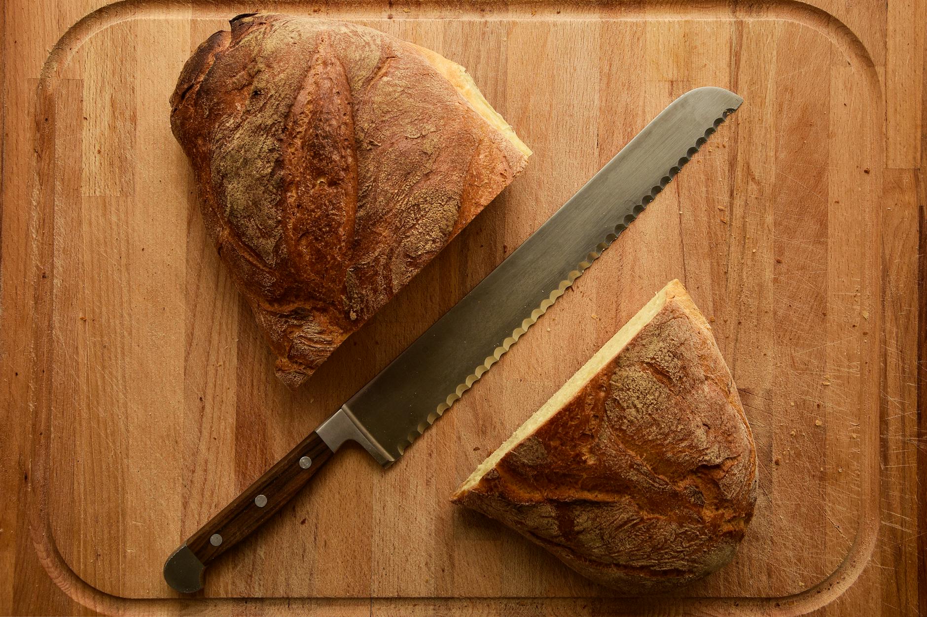 Serrated Bread Knife On A Cutting Board With Crusty Bread And Ripe Tomatoes