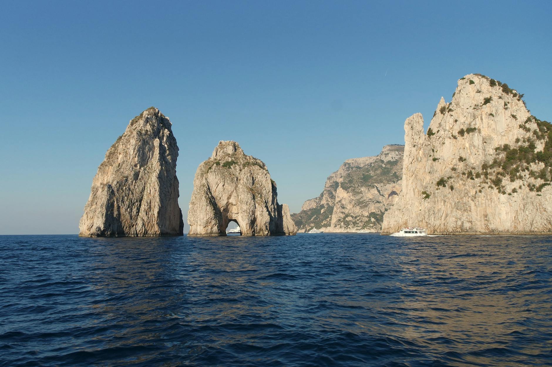 Capri Island With Blue Grotto, High Cliffs, Faraglioni Rock Formations, And Vibrant Bougainvillea Flowers